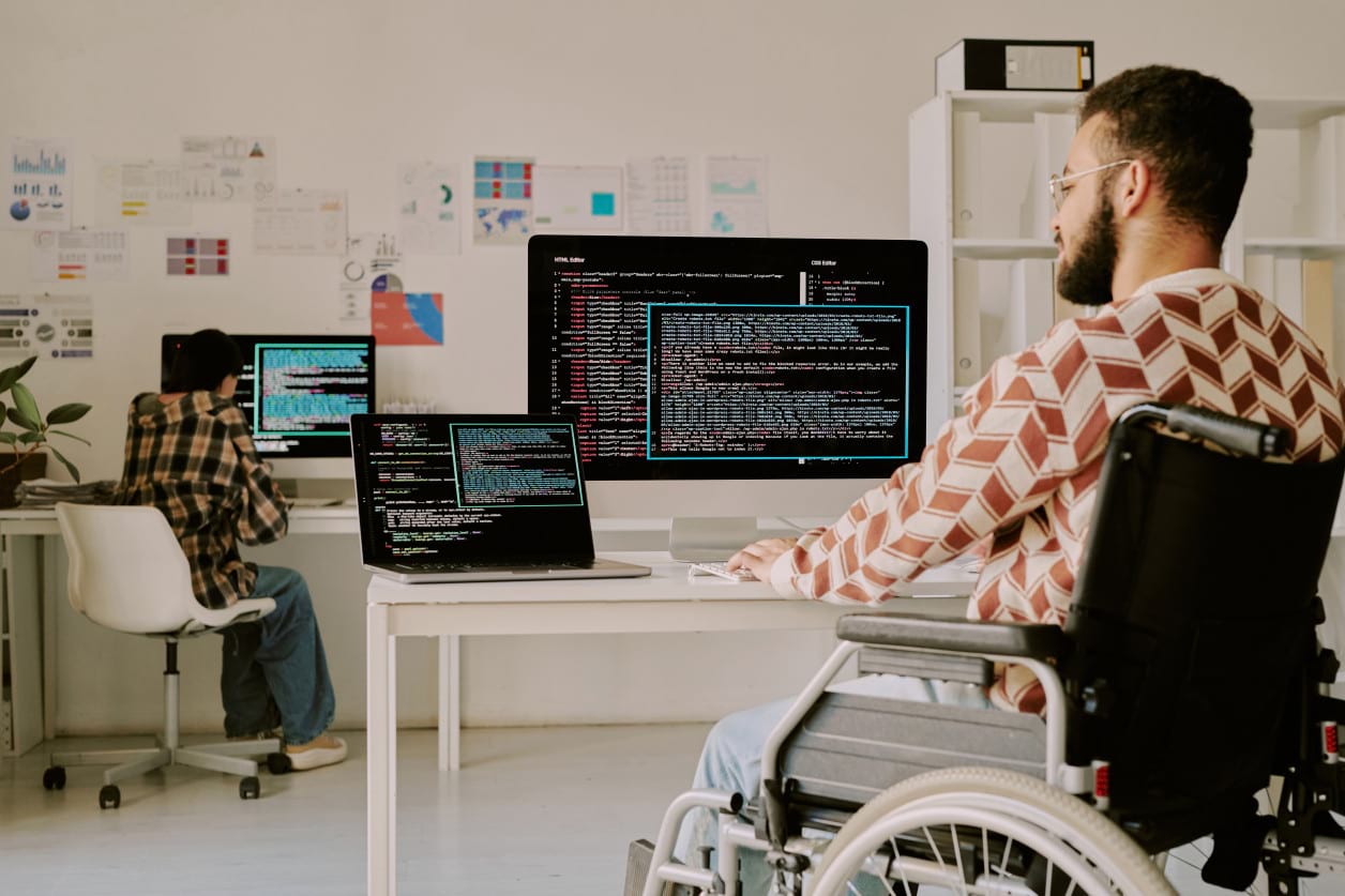 Smiling student in wheelchair coding Python on laptop during Pitman Training IT Specialist course