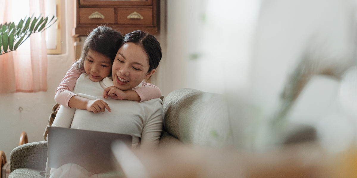 A smiling mother embraces her child on a sofa in their living room while planning her guide to returning to work journey